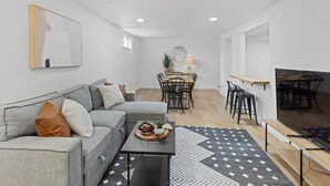 Ein modernes Wohnzimmer mit grauem Sofa, einem Couchtisch und einem Essbereich mit Tisch und Stühlen.