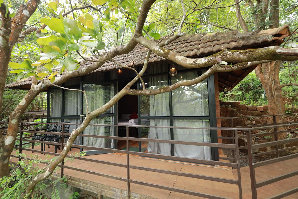 Uma casa na árvore com design rústico, apresentando um deck de madeira e uma porta de vidro que dá acesso a um quarto.