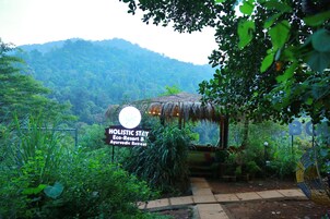 A sign for Holistic Stay Eco-Resort & Ayurvedic Retreat surrounded by lush greenery and a thatched-roof structure.