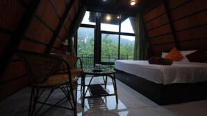 A room with a bed, a table, and chairs. There is a window with a view of greenery outside. - Holistic Stay Eco Resort (Talipparamba)