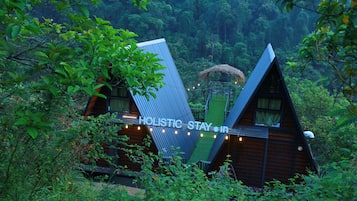 A wooden cabin with a sloped roof, surrounded by dense forest.