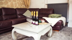 A living room with a brown leather sofa, a white coffee table with wine bottles and glasses, and a green pillow on the sofa. - Le Paradis des Bulles (Lisse-en-Champagne)