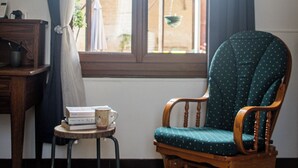 A wooden rocking chair with a green cushion, a small wooden table with a mug and a book, and a woven rug on a tiled floor. - Le Paradis des Bulles (Lisse-en-Champagne)