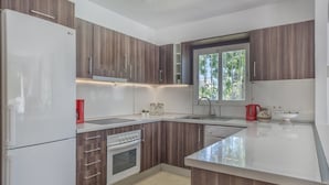 A modern kitchen with wooden cabinets, a white refrigerator, a built-in oven, and a large island with a sink. - 3 bedroom with private garden walking distance to everything (Marbella)