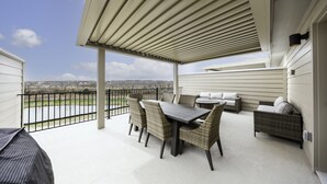 Eine überdachte Terrasse mit Tisch, Stühlen, einer Couch und einem Grill.