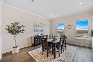 A dining area with a table, chairs, a potted plant, a painting, and a window with a view.