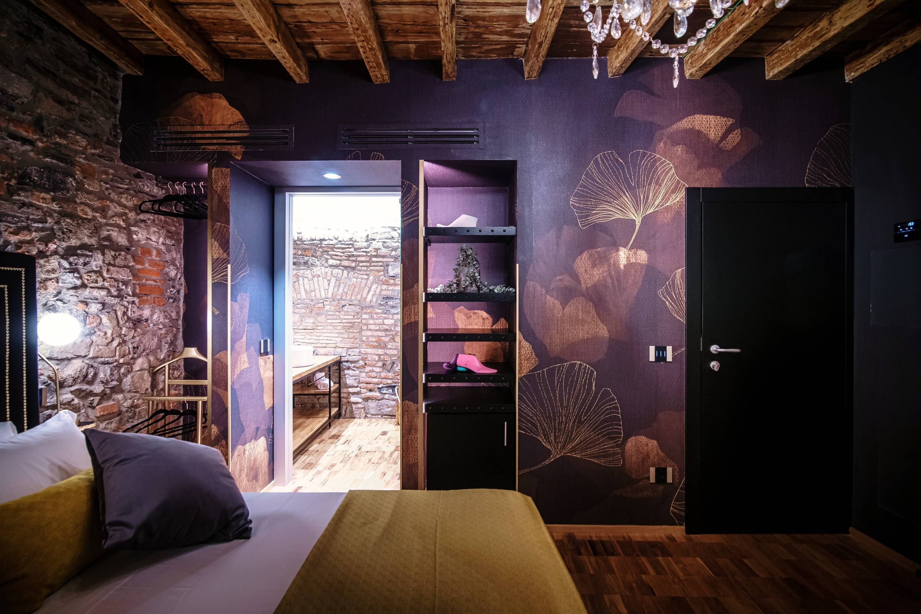 Ein Schlafzimmer mit einem Bett, Holzboden, Steinwand, einem Regal mit Dekoration und einer Tür.