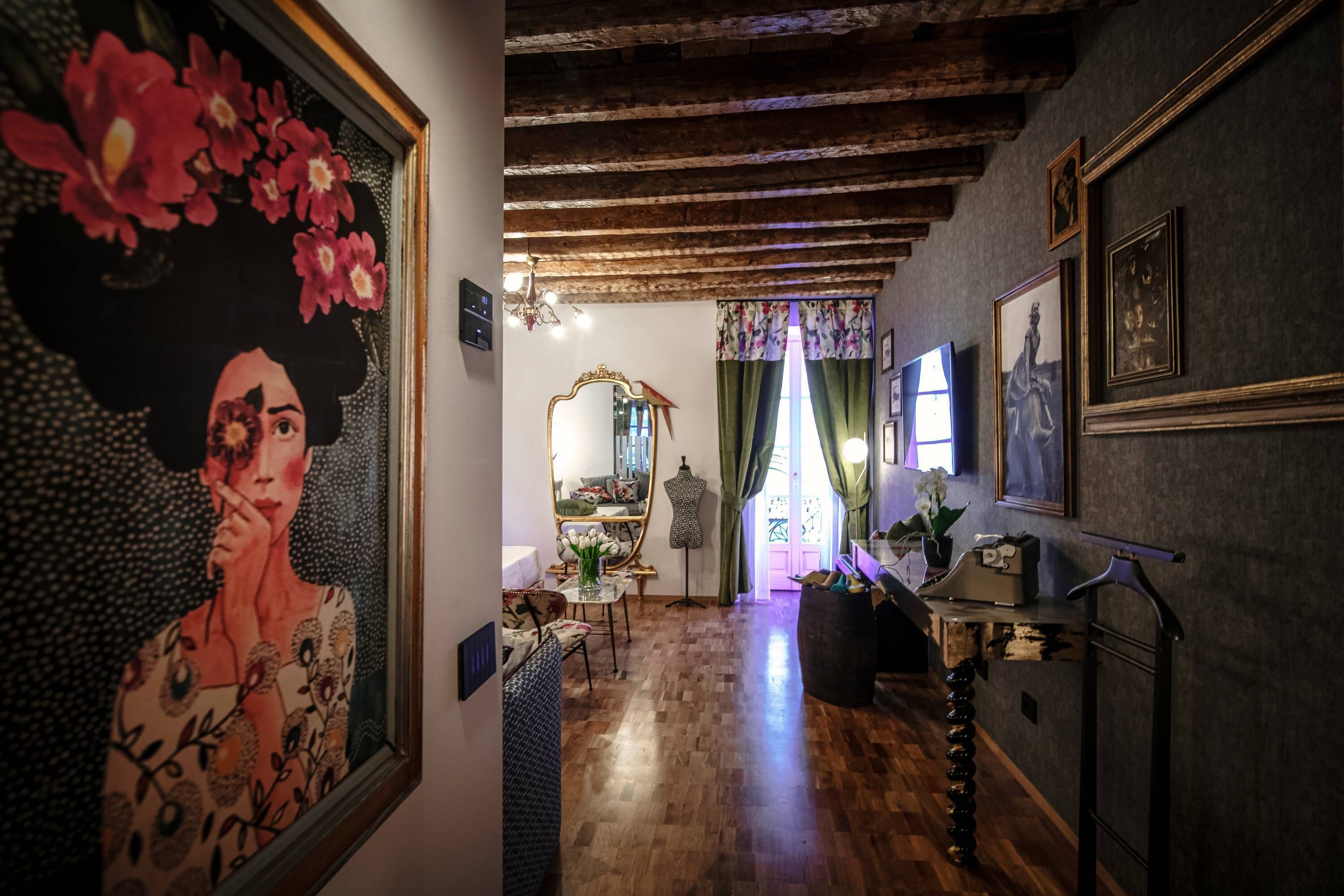 Un pasillo con suelo de madera, un espejo, un maniquí y una mesa con un florero.