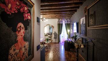 Un pasillo con suelo de madera, un espejo, un maniquí y una mesa con un florero.