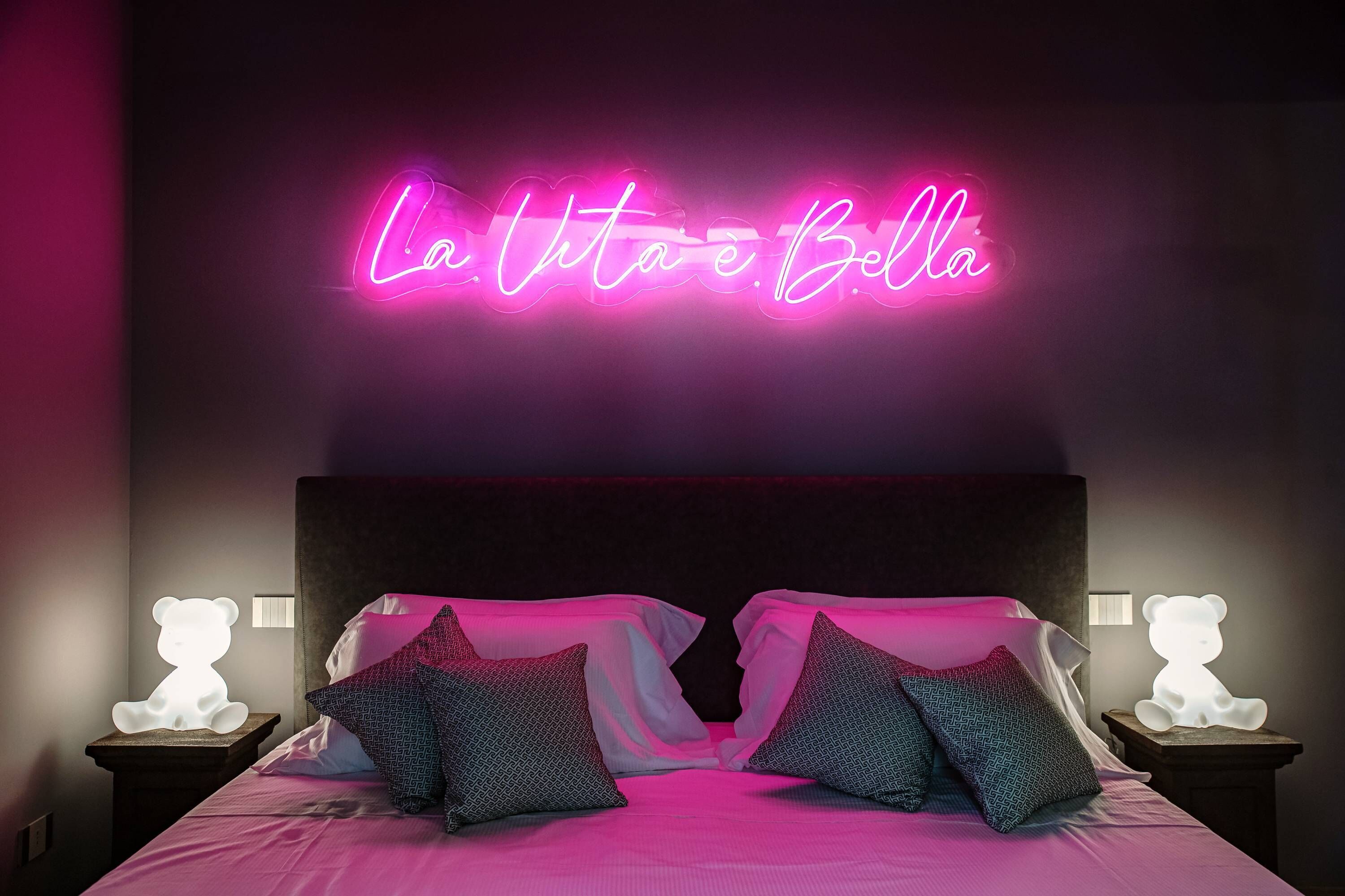 A bedroom with a bed, two bedside tables, and a neon sign above the bed.
