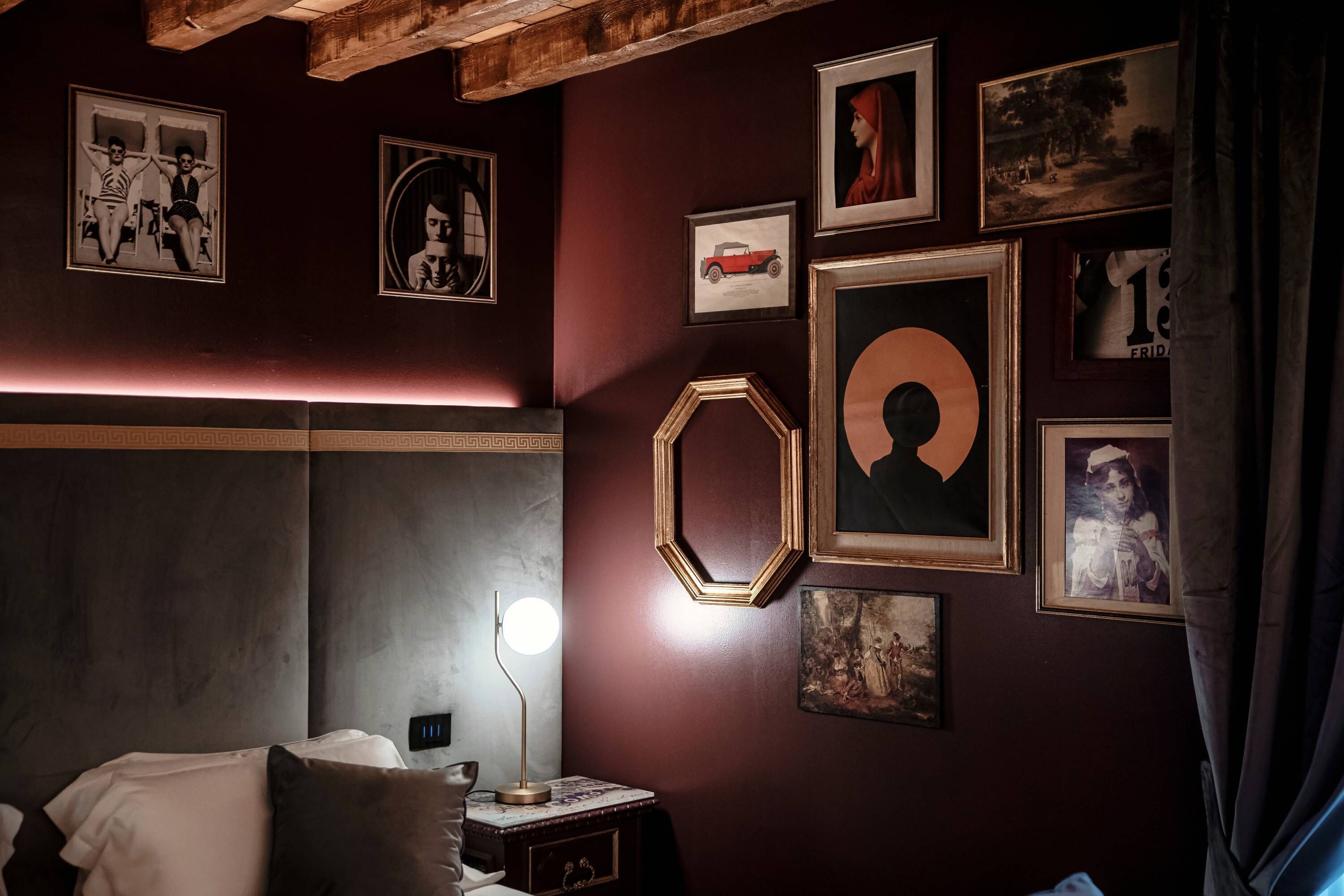 A room with a bed, a nightstand with a lamp, and various framed pictures on the wall.