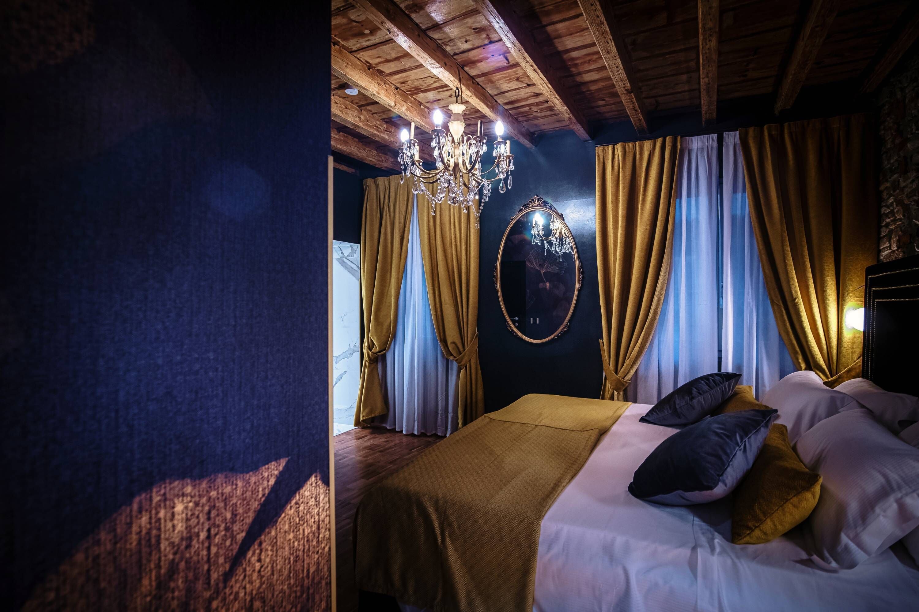 A bedroom with a wooden ceiling, a chandelier, a bed with multiple pillows, and curtains.