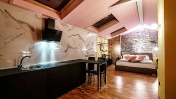 Una cucina moderna con schienale in marmo, pavimento in legno e isola integrata. Si notano in secondo piano un muro in pietra e un letto con cuscini.