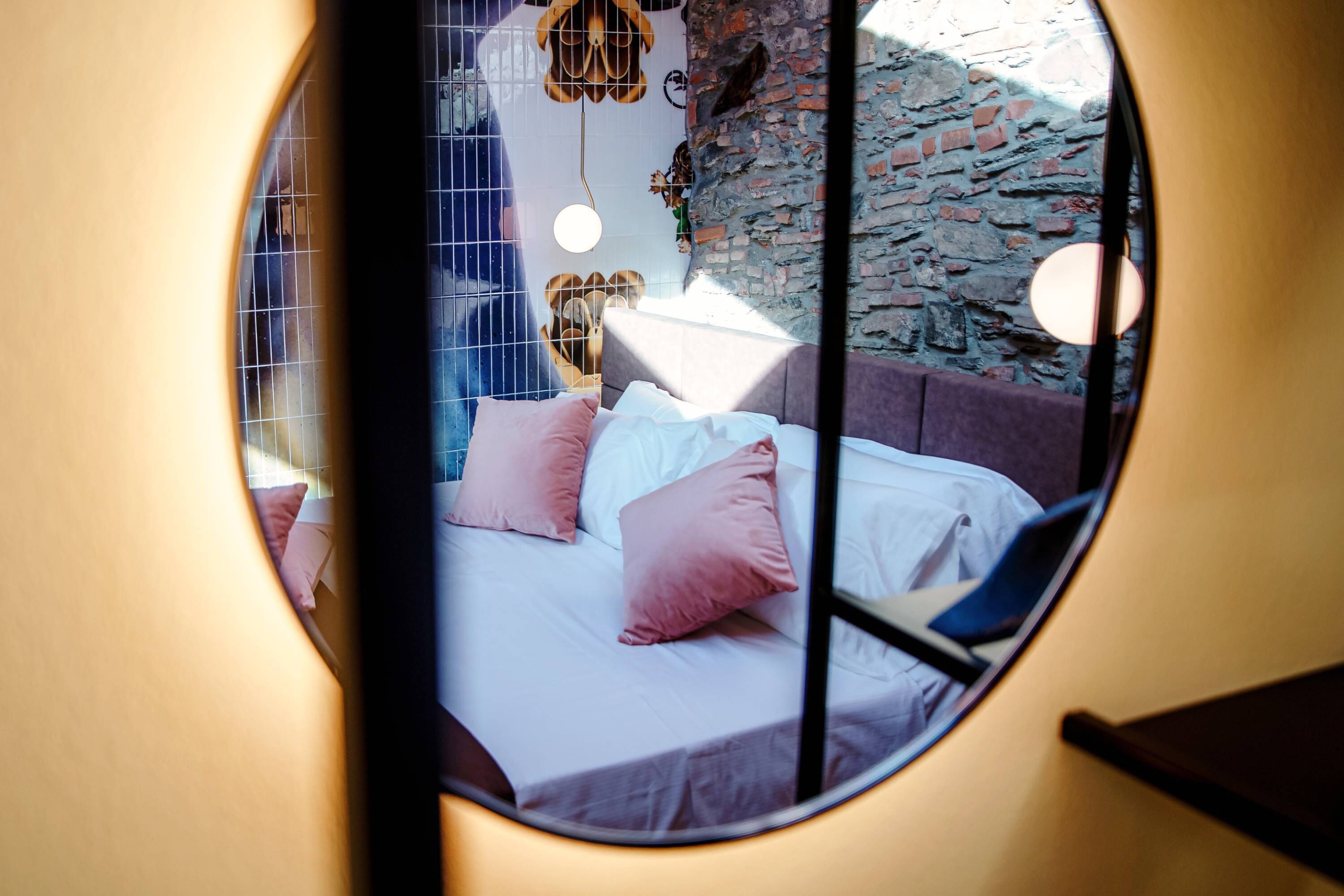 Vista circular desde una ventana de un dormitorio con cama, almohadas y lámparas colgantes.