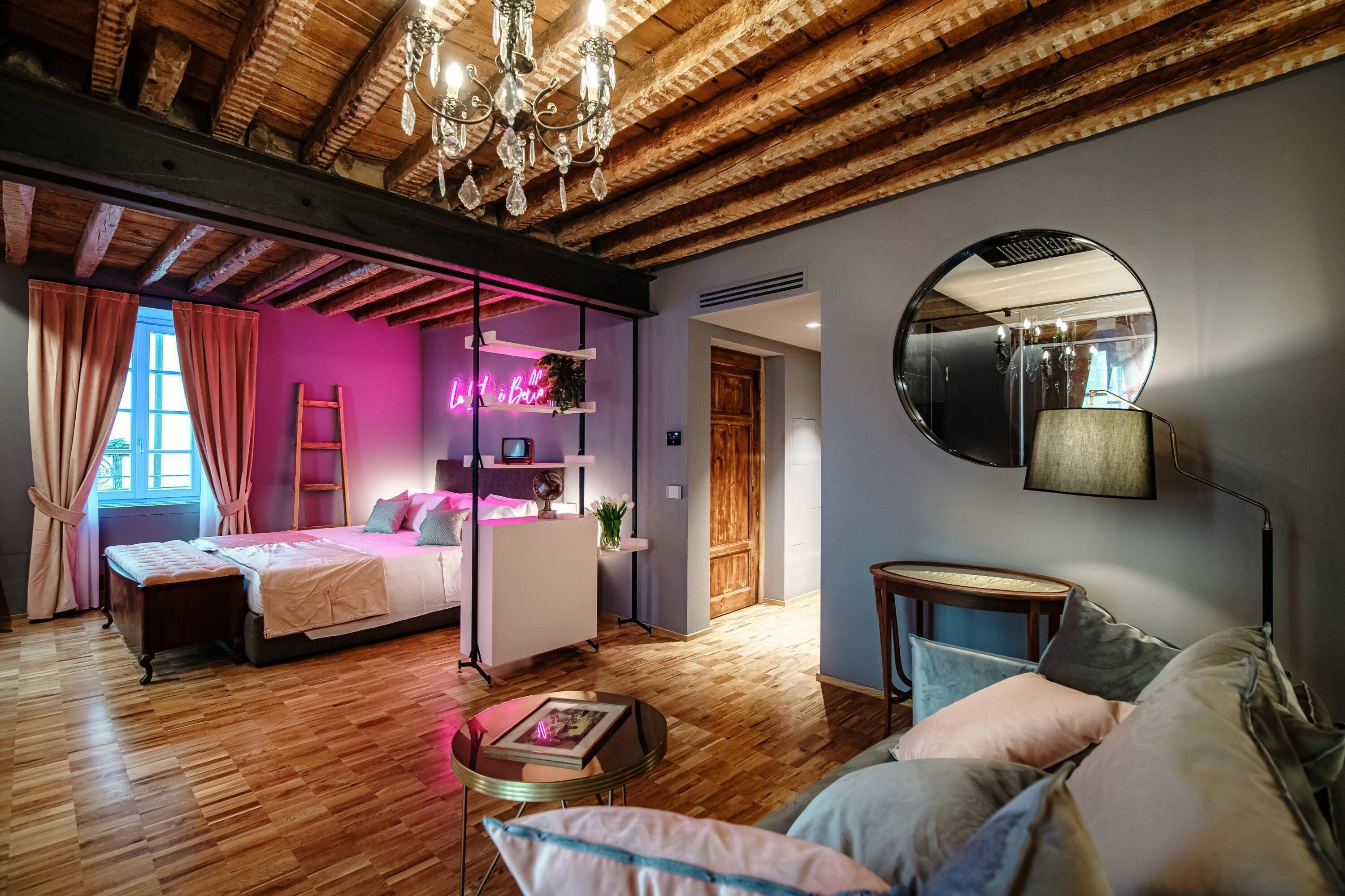 Ein Zimmer mit Holzboden, einem Bett, einem Schreibtisch, einem runden Spiegel und einer Couch.