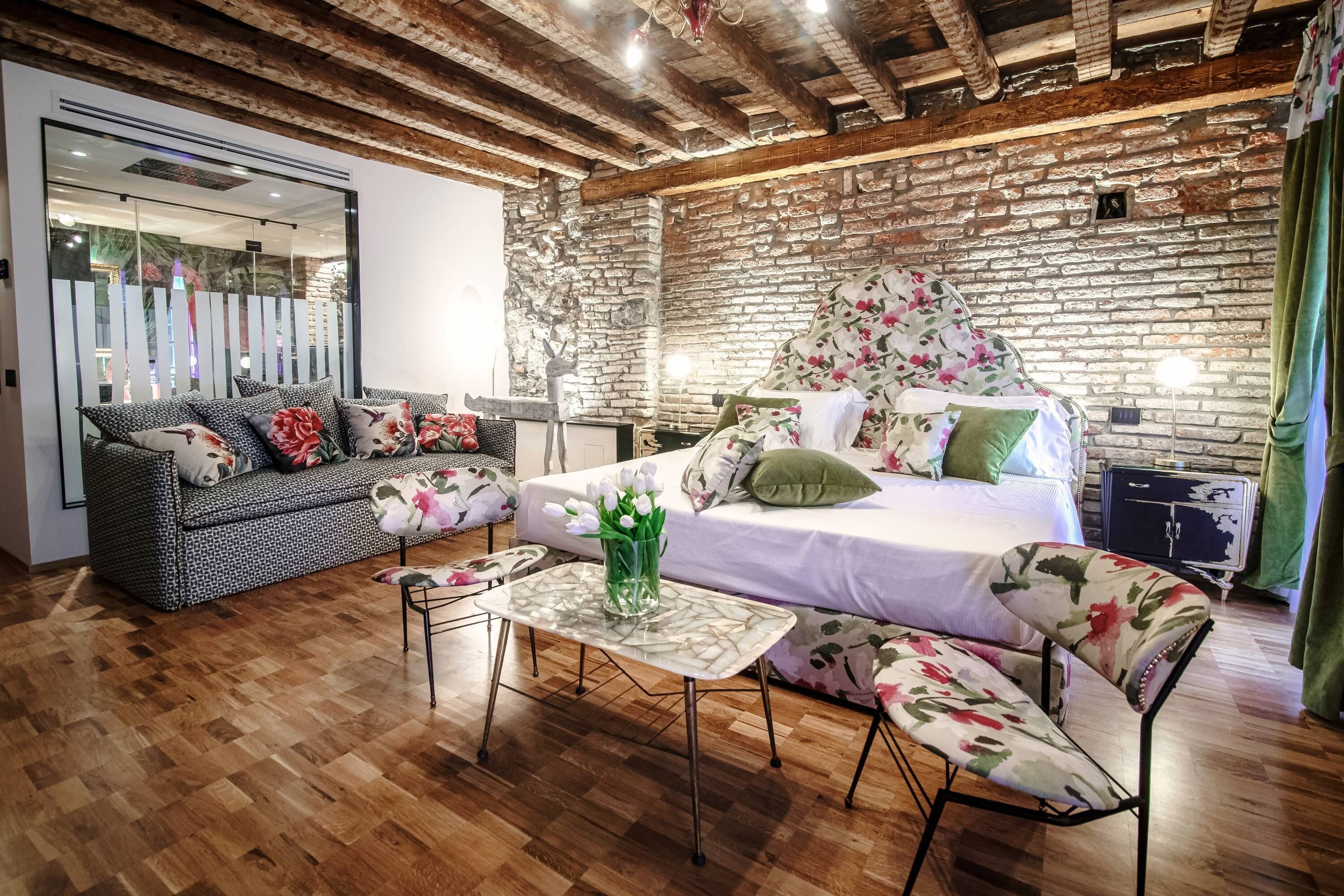 Una habitación acogedora con una cama, un sofá y una mesa. El suelo es de madera y la pared de ladrillo.
