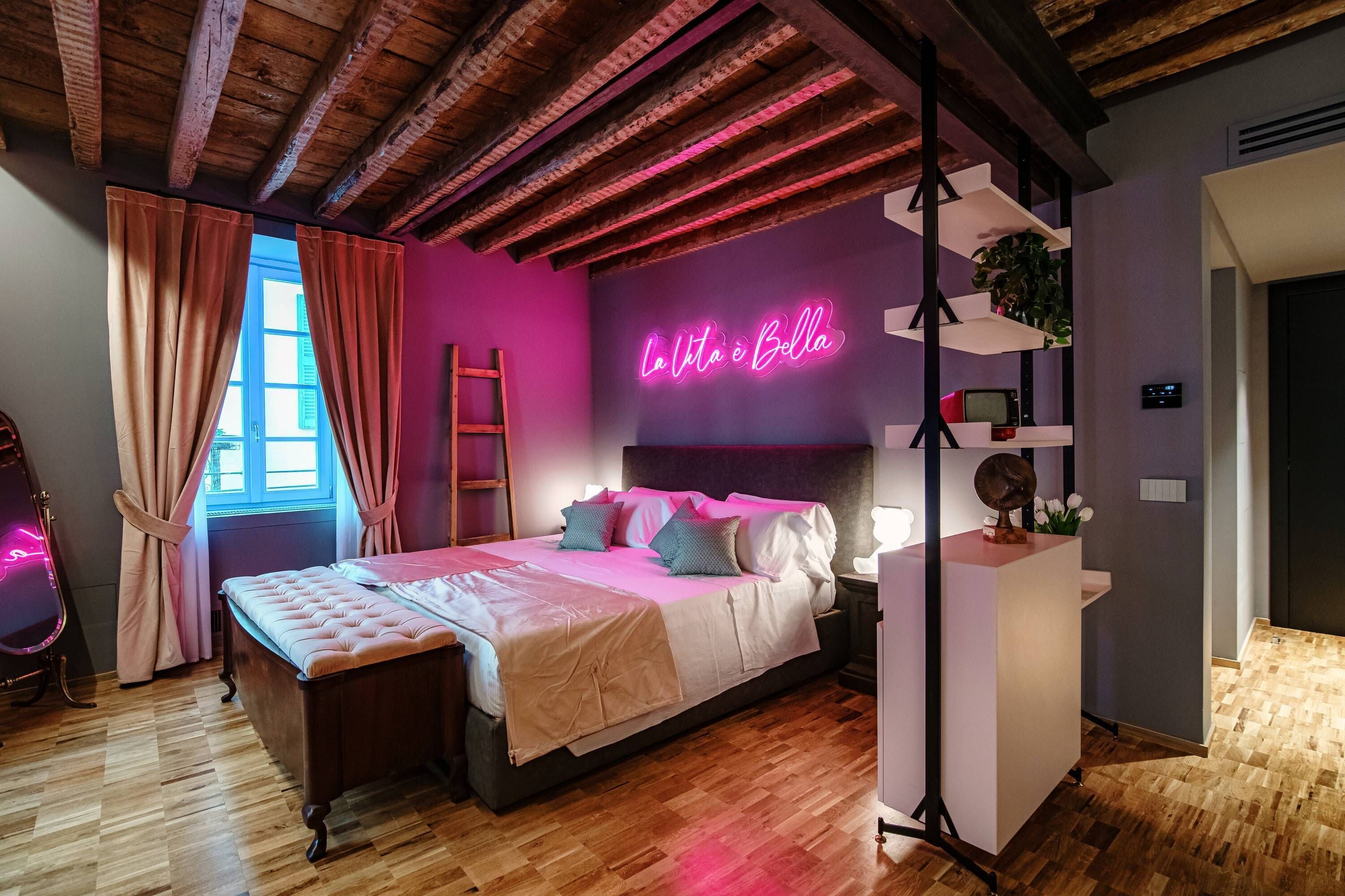 A bedroom with a bed, a vanity, a neon sign, and a window with curtains.