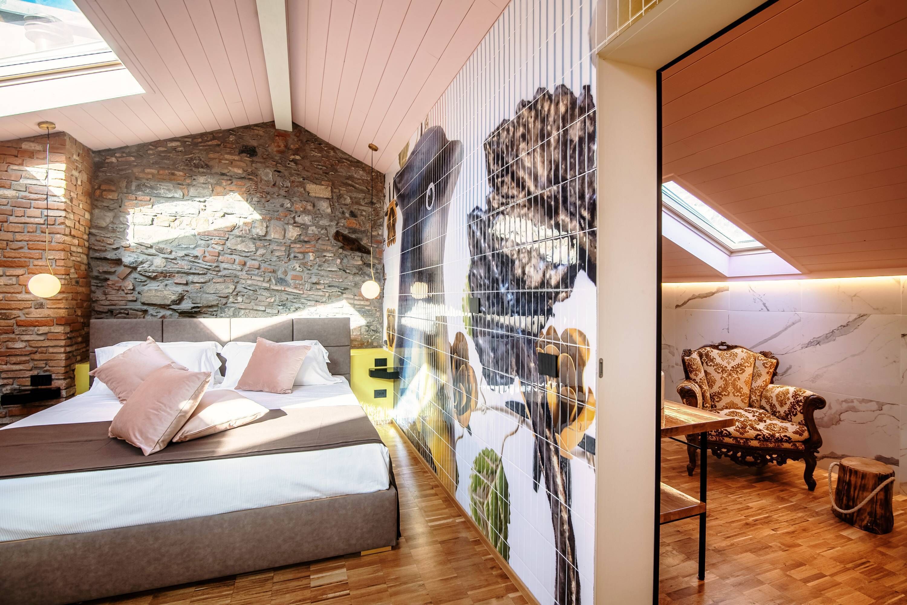 Camera da letto con parete in pietra, un letto con cuscini, una sedia e un affresco con uccelli.