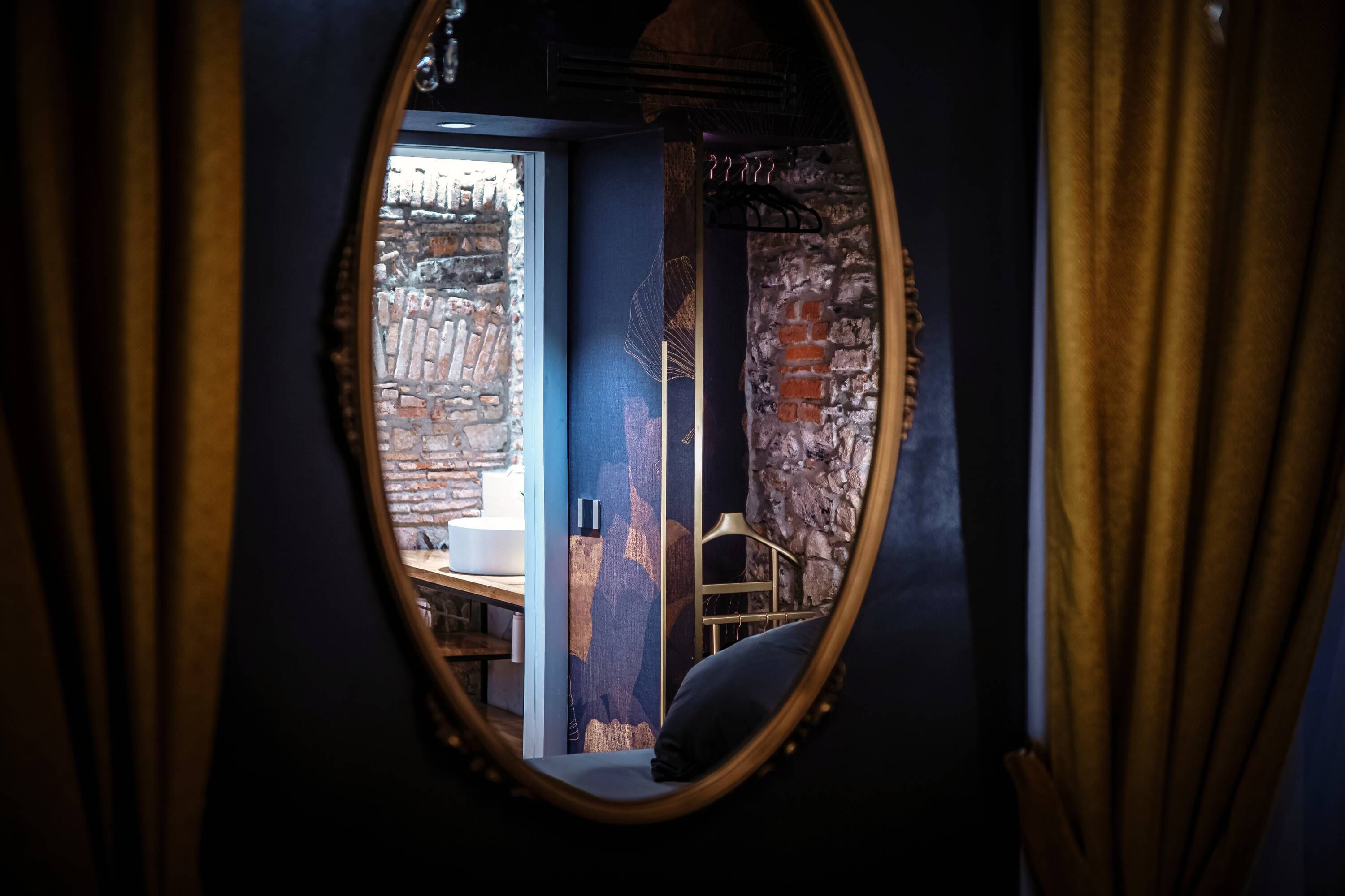 An oval mirror reflecting a room with a brick wall, a wooden chair, and a window.