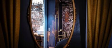 An oval mirror reflecting a room with a brick wall, a wooden chair, and a window.