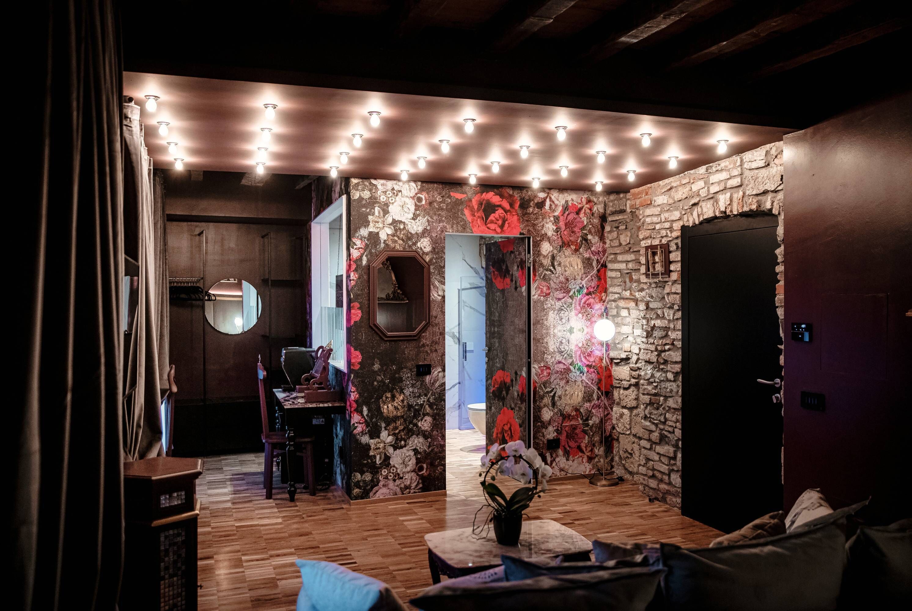 Ein gemütliches Zimmer mit Holzboden, einer Steinwand mit Blumenwallpaper, einem Spiegel und einer Tür.