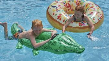 Dos niños flotando en una piscina con juguetes inflables, uno con forma de cocodrilo y el otro de rosquilla.