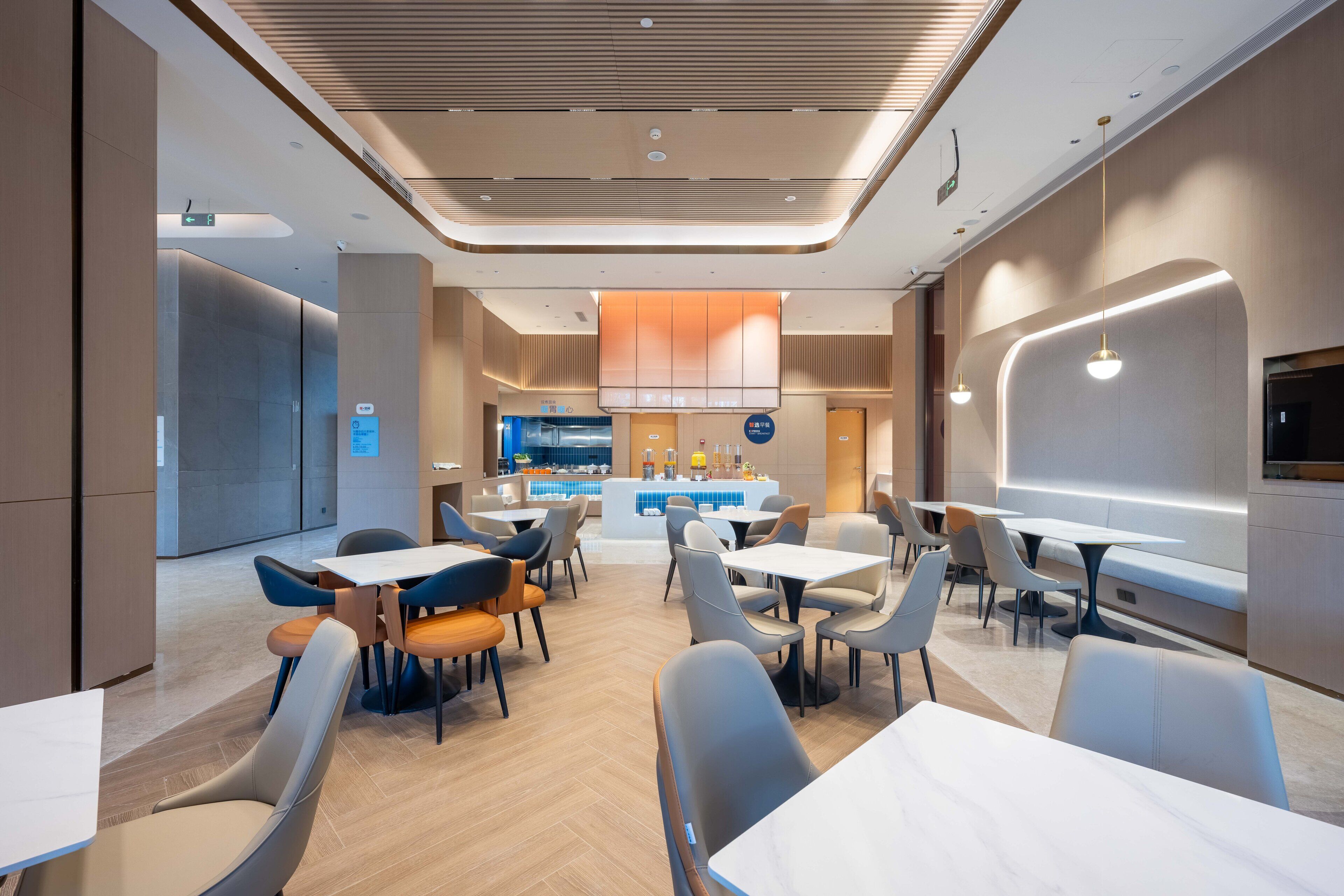 Un espace repas moderne avec des tables et des chaises, un bar central et une piscine visible au fond.
