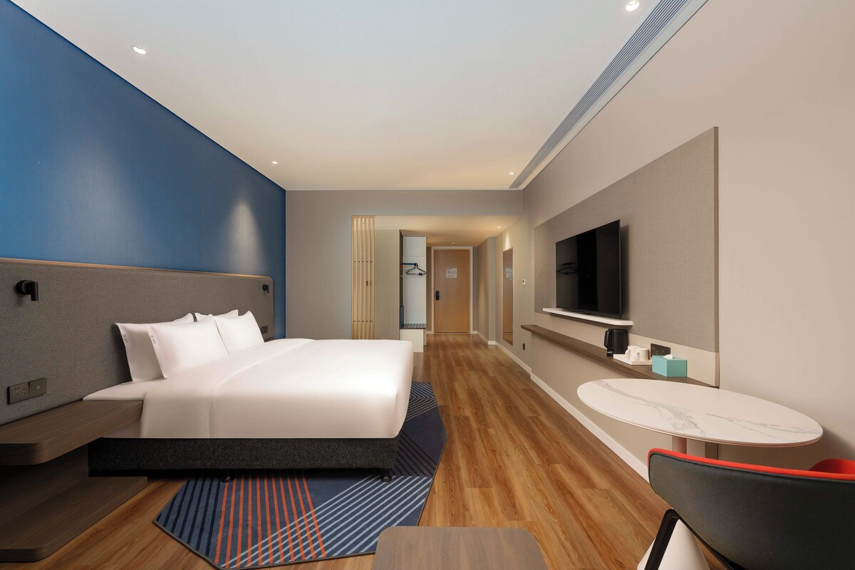 A modern hotel room with a bed, a TV, a small table, and a chair.