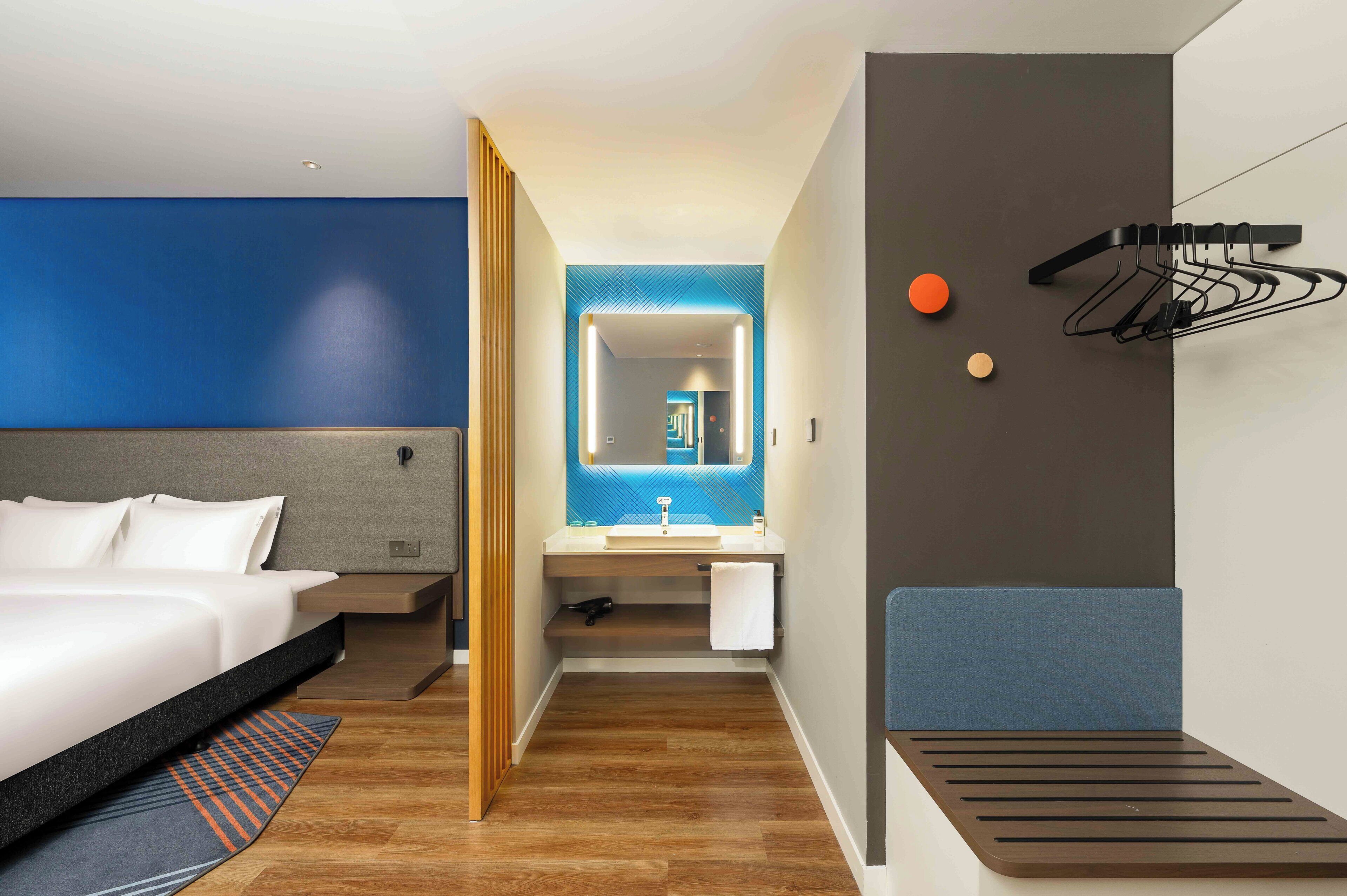 A modern hotel room with a bed, a bathroom, and a seating area.