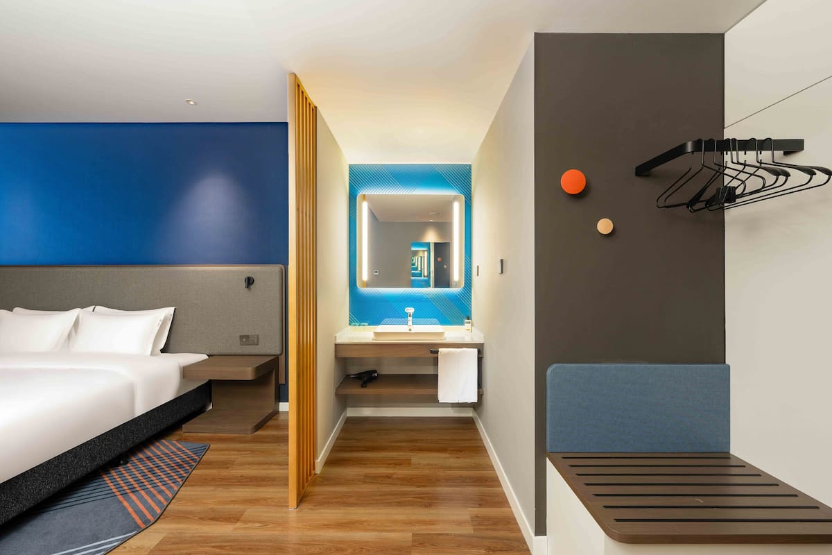 Ein modernes Hotelzimmer mit einem Bett, einem Badezimmer mit Spiegel und einem an der Wand befestigten Handtuchhalter.
