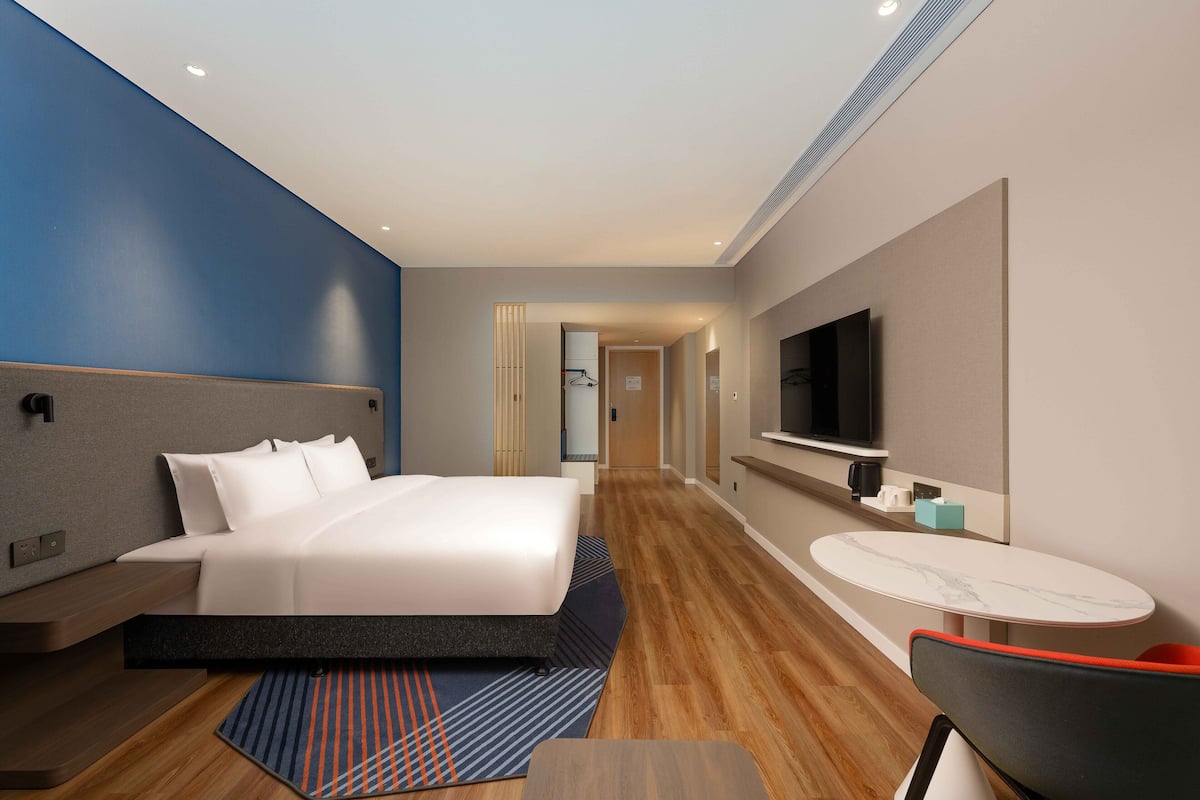 Ein modernes Hotelzimmer mit einem Bett, einem Fernseher, einem kleinen Tisch und einem Sessel.