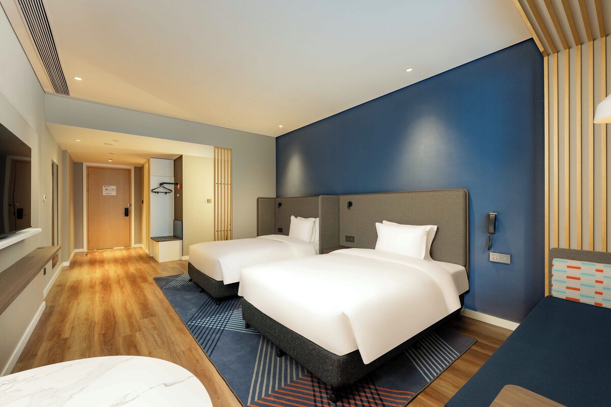 A hotel room with two beds, a desk, and a TV.