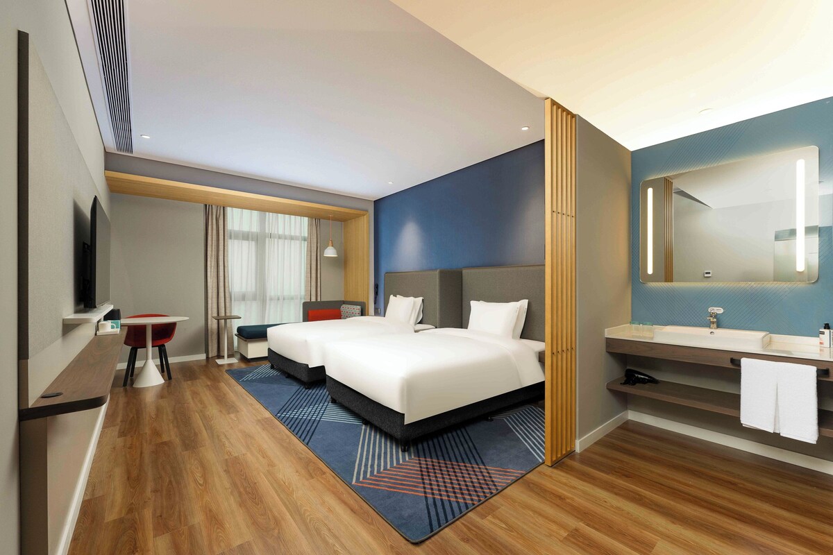 A hotel room with a large bed, a desk, a chair, a bathroom with a mirror and sink.
