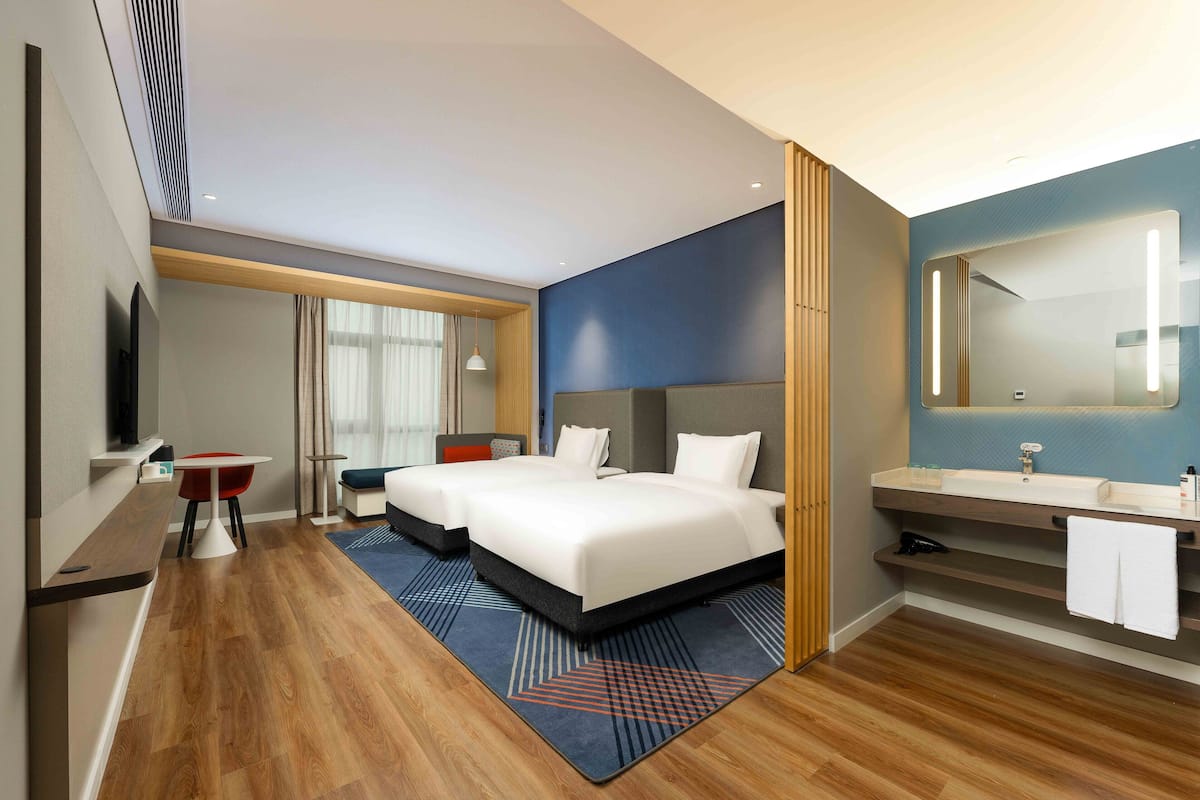 Ein Hotelzimmer mit einem großen Bett, einem Schreibtisch, einem Stuhl und einem Badezimmer mit Spiegel und Waschbecken.