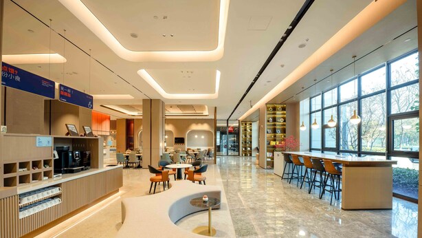 A modern hotel lobby with a reception desk, seating area, and large windows offering natural light. - Holiday Inn Express Haiyan by IHG (Jiaxing)