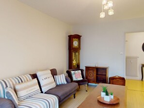 A living room with a sofa, a wooden cabinet, a clock, and a table with plants.
