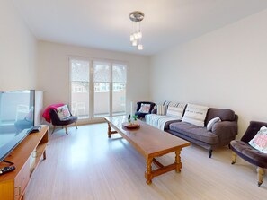 A living room with a wooden coffee table, a sofa, a TV, and a balcony with large windows.