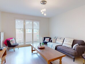 A modern living room with a wooden coffee table, a grey sofa with striped pillows, a black armchair, and a large window with a view of buildings.