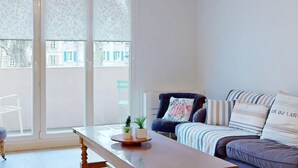A modern living room with a sofa, a chair, a table, and a view through a large window. - Modern Apartment with Balcony in Colmar Center near Museum, Parking Included (Colmar)
