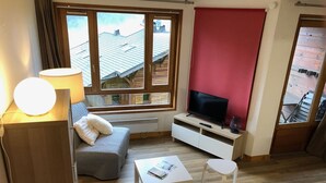 Una sala de estar acogedora con un sofá, un televisor, una lámpara y una ventana con vistas a una terraza de madera.