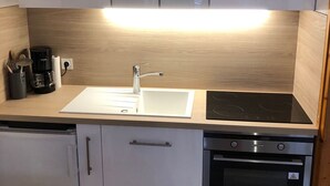 Una cocina moderna con gabinetes blancos, un lavamanos de acero inoxidable, una cafetera y un horno empotrado.