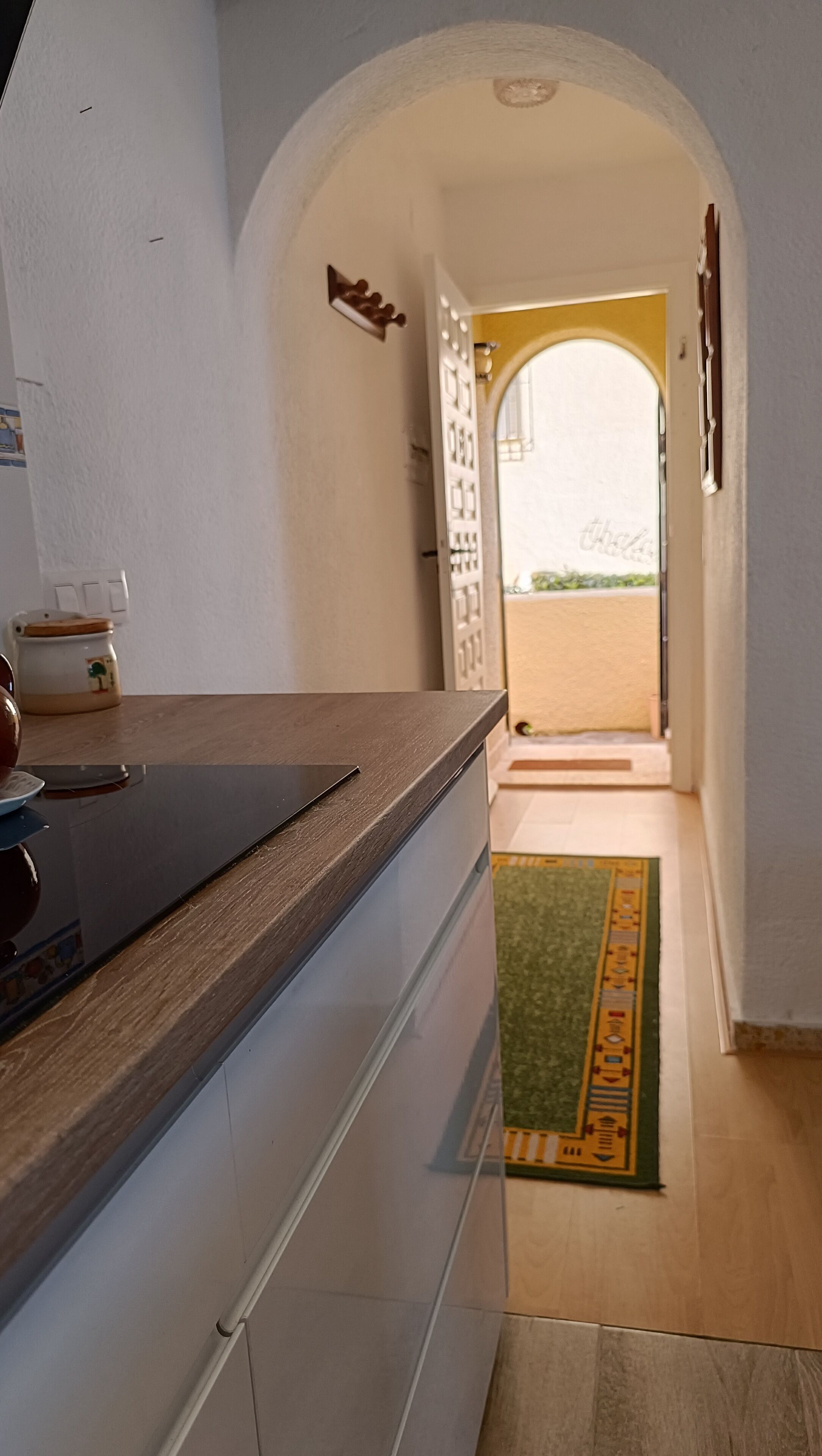 A kitchen with a wooden countertop, a sink, and a view of a balcony through an open doorway.