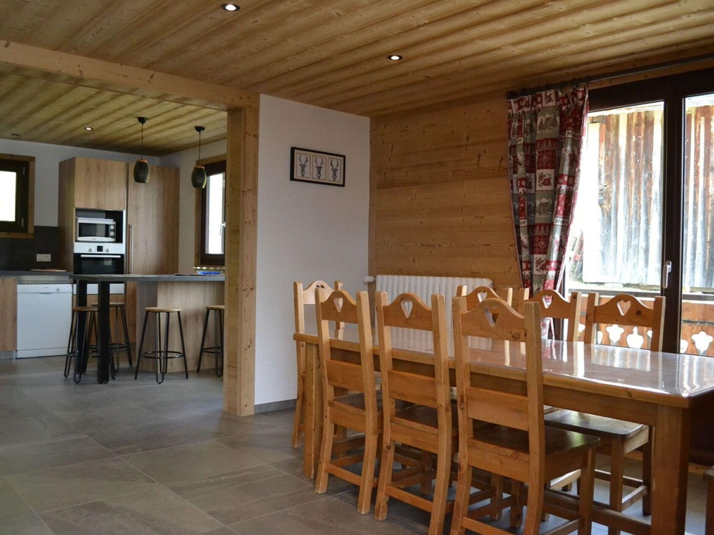 A wooden interior with a dining table and chairs, a kitchen area with a microwave, and a window with curtains.