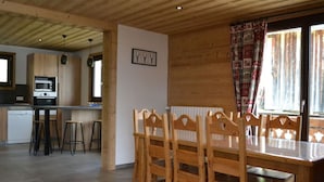 A wooden interior with a dining table and chairs, a kitchen area with a microwave, and a window with curtains. - Chalet 3 bedrooms, balcony, parking, pets allowed, 8 ppl. (Châtel)