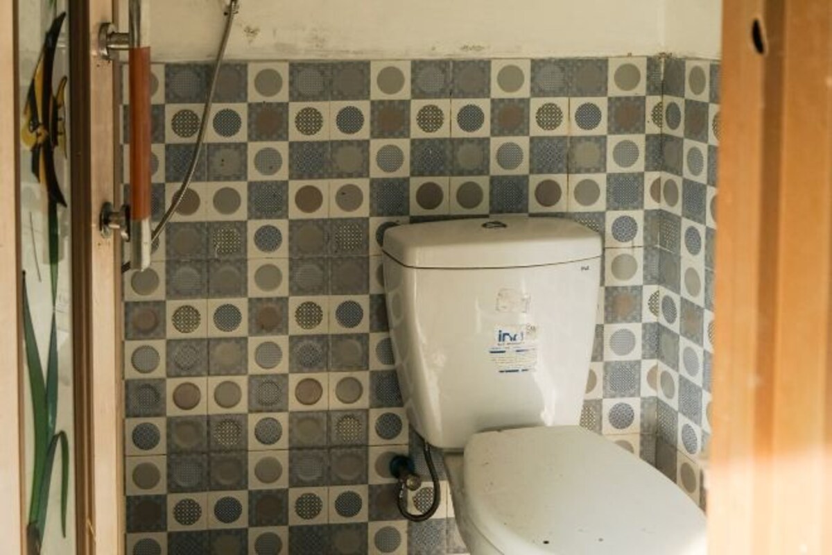 A bathroom with a toilet, a tiled wall with a checkered pattern, and a shower area with a showerhead.