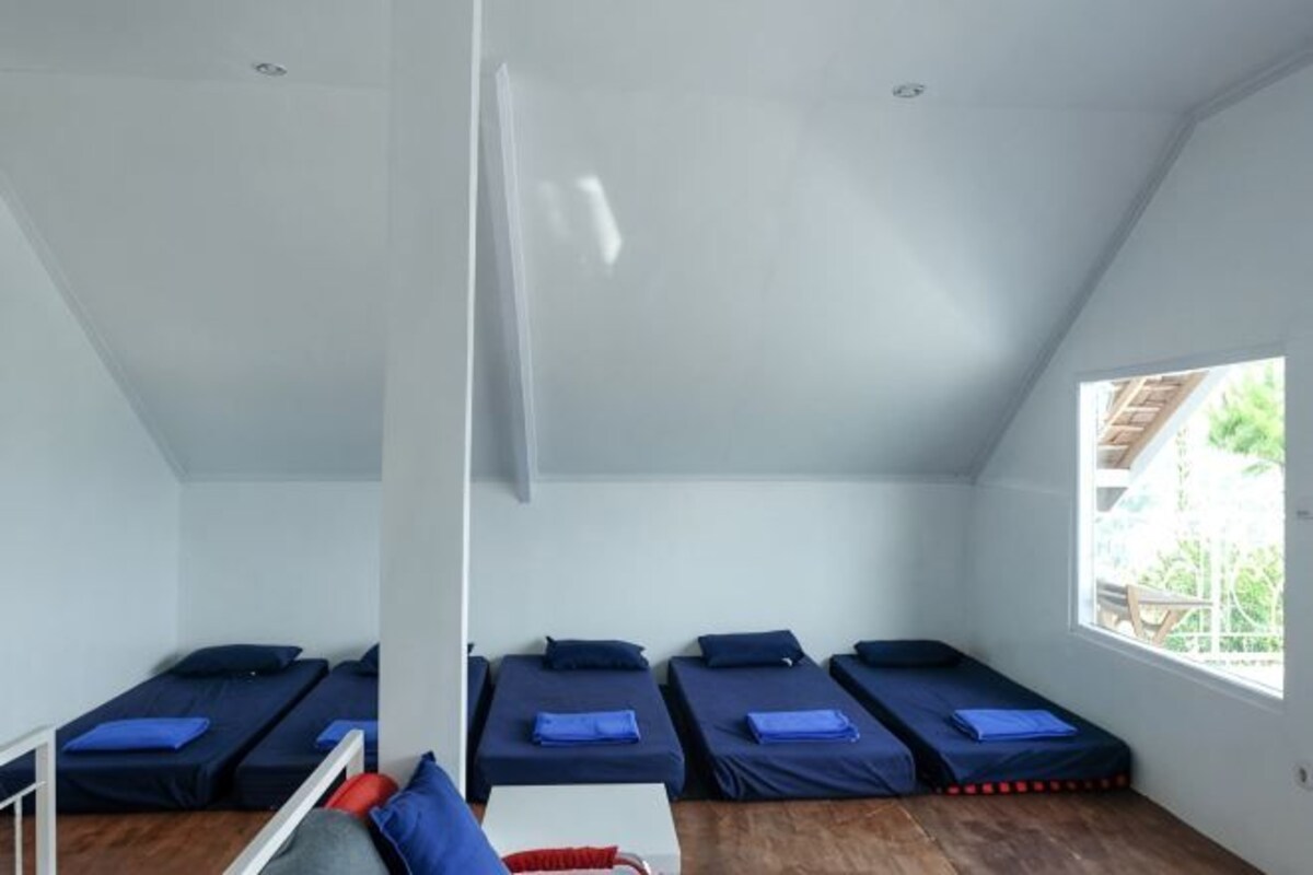 A room with four single beds arranged in a row, a window, and a wooden floor.