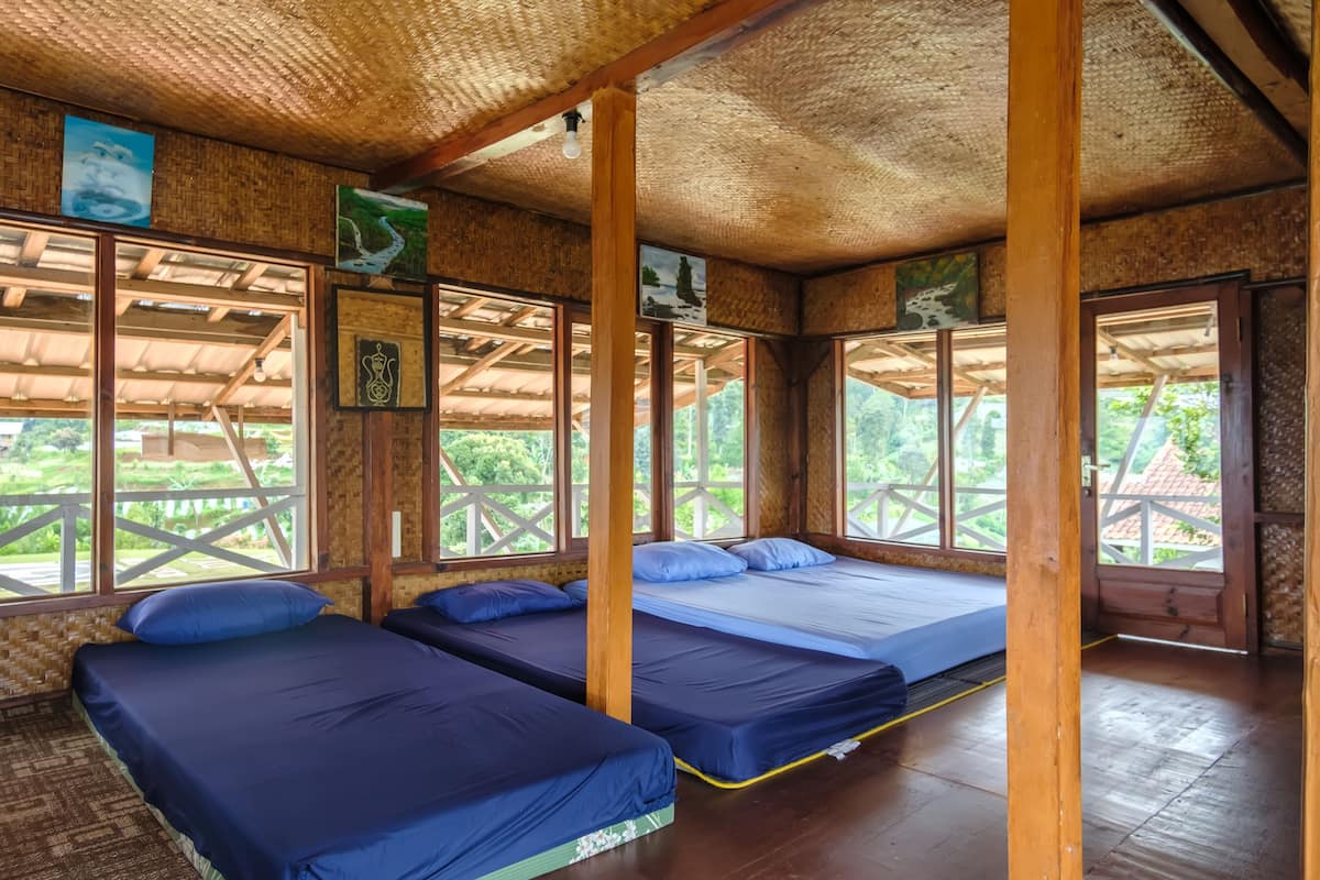 Ein Zimmer mit zwei Einzelbetten, Holzbalken, großen Fenstern und einem Strohdach.