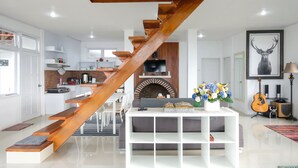 A modern living room with a wooden staircase, a fireplace, a sofa, and a coffee table with flowers. - Hilltop Camp, Lembang (Lembang)