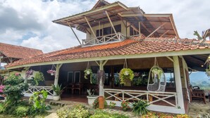 Una casa con techo de tejas, un balcón con plantas colgantes y un jardín con diferentes macetas.