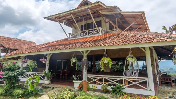A house with a tiled roof, a balcony with hanging plants, and a garden area with various potted plants. - Hilltop Camp, Lembang (Lembang)